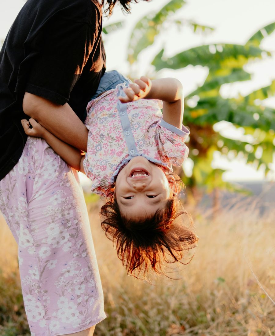 A laughing child held upside down by her mother in golden light